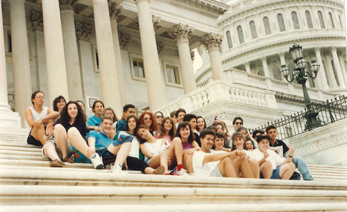 A diverse crowd of people celebrating at a concert, raising their hands and cheering.